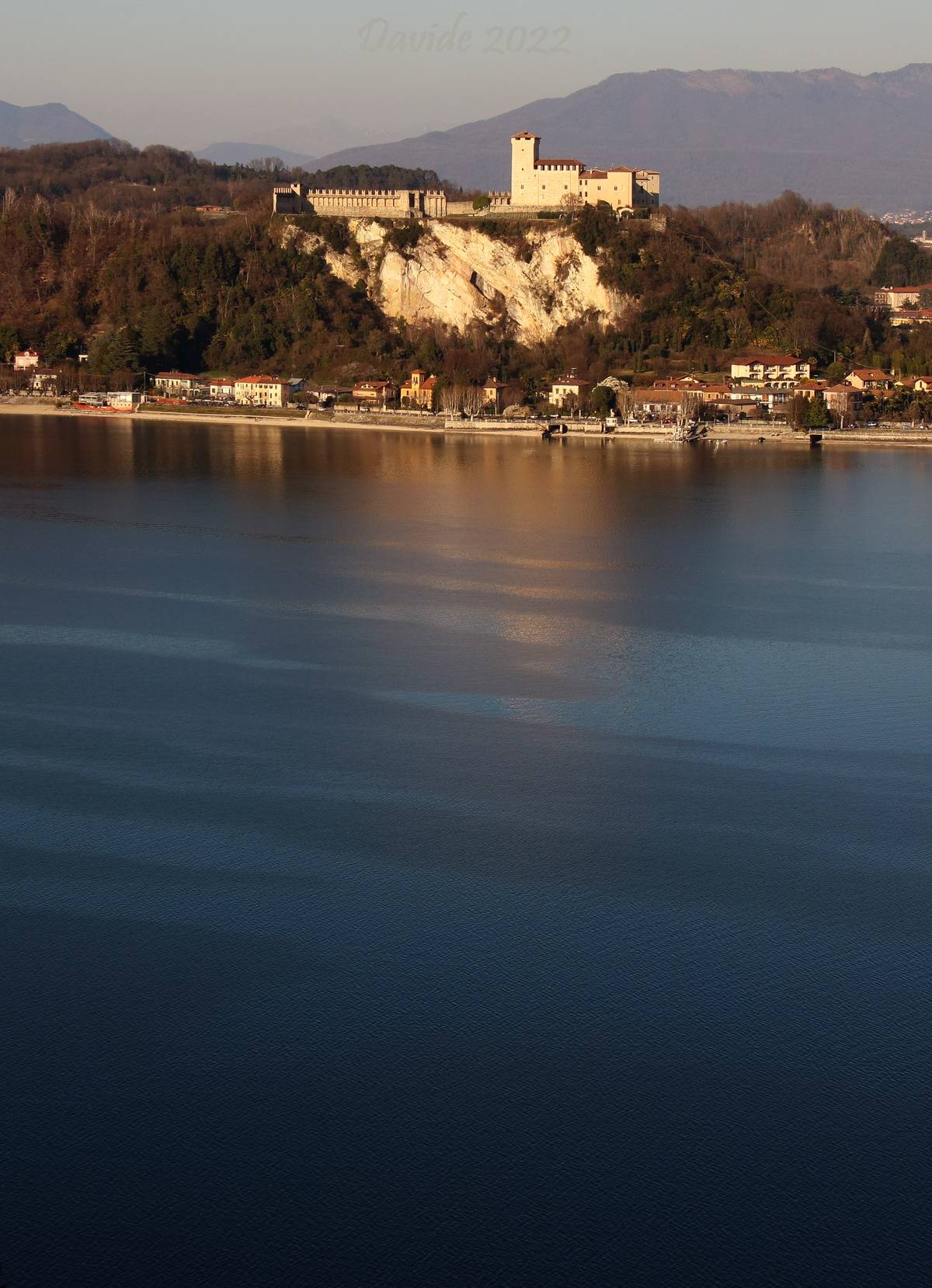 Arona (Novare, Piémont – Lago Maggiore, Italie). Vue du bas lac Majeur et de la rive de Varese avec la Rocca Borromeo d’Angera (image prise du parc de la Rocca Borromea d’Arona). Davide Tansini. 2022. Photographie numérique